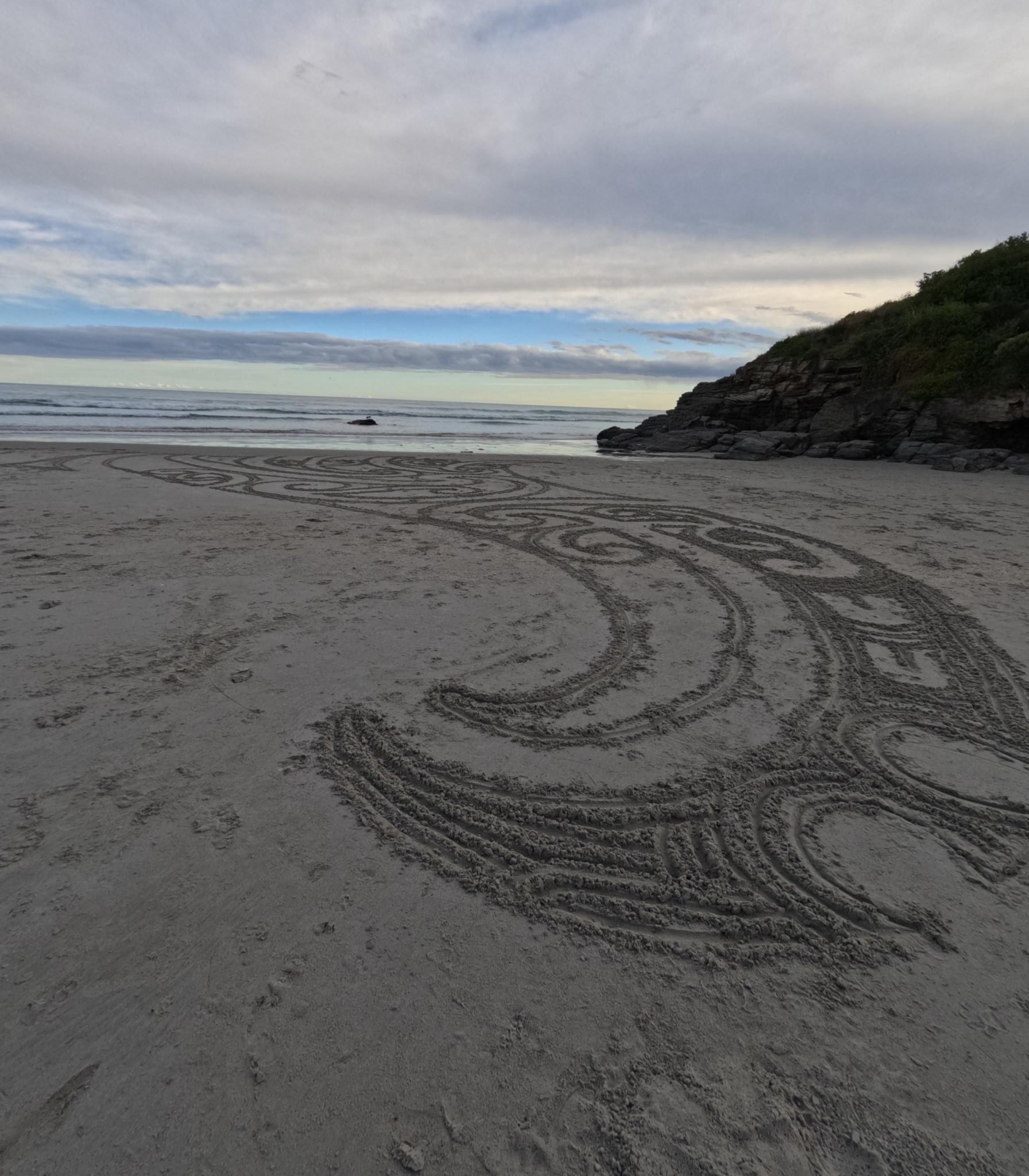 A photo of Māori art in the sand with ocean in the background.